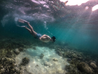 Side view of man free diving  under the dark sea with coral and reef.