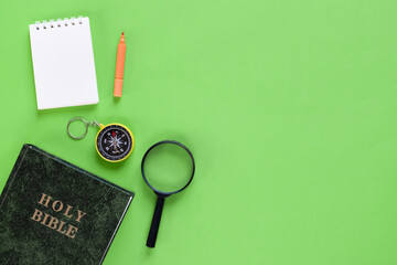 Top view of Holy Bible, compass, magnifying glass, and mini notebook on green background