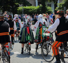 Local people in traditional folk costumes from Lowicz, Poland, ride bicycles in street while celebrate Corpus Christi holiday