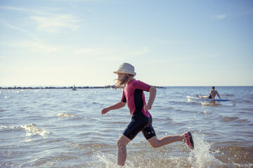 Happy pretty teen girl in neoprene swimingsuit  running in Baltic sea