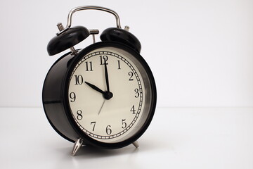 Naklejka premium Black vintage alarm clock on table. White background. Wake up concept. An image of a retro clock showing 10:00 pm/am. 