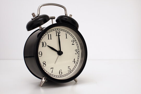 Black vintage alarm clock on table. White background. Wake up concept. An image of a retro clock showing 10:00 pm/am. 