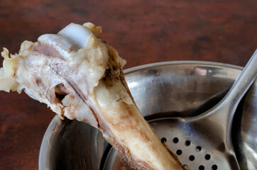 Boiled beef bone in a metal bowl with a slotted spoon.