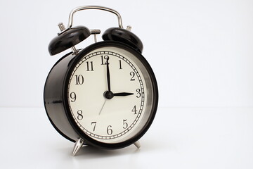 Black vintage alarm clock on table. White background. Wake up concept. An image of a retro clock showing 03:00 pm/am. 