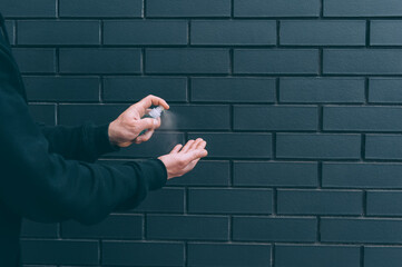Man disinfecting his hands with blue hand sanitizer from a bottle on brick background.