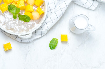 The thai dessert food modern style : The homemade sago in coconut milk with topping is mango cut into squares and cantaloupe ball in the white bowl and placed on tablecloth plaid on the marble table.