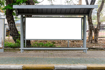 The empty blank white mock up billboard at the bus stop in the city park. In mock up billboard for ads, advertising, maps of buses and street next to road.