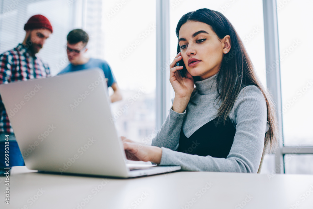 Aufkleber serious businesswoman calling on smartphone while checking email on laptop computer using wireless i