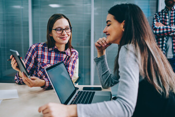Positive colleagues discussing funny video on modern touch pad during collaboration on common...