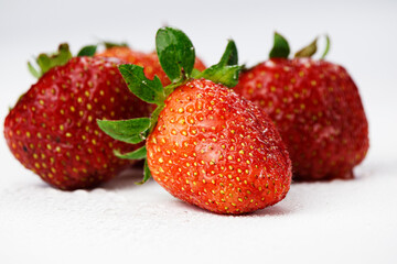 Four strawberries in earthen crumbs on a white background.