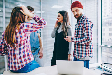 Male and female students casual dressed standing at modern office and talking about studying in break of e learning, group of positive millennial teenage friends discussing cours work indoors