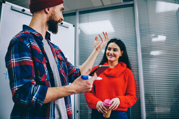 Successful bearded male speaker holding touch pad and gesturing with hand during conducting interesting workshop for positive hipster students in classroom.Professional coach discussing strategy