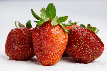 Four organic strawberries with water droplets on a white background.