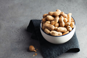 A lot of roasted peanuts in shell in a bowl on a gray background. Healthy eating concept. Copy space. Foodphoto.