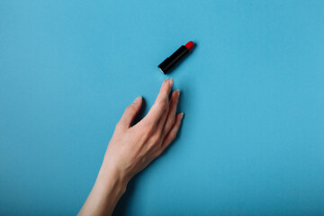 The woman's hand is taking red lipstick. isolated On the blue background