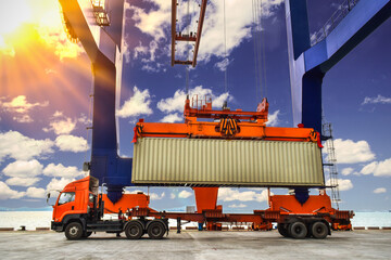 Quay crane lifting up 40 feets container from trailer using spreader at container port with blue sky background and backlight. Container loading unloading activities at seaport.