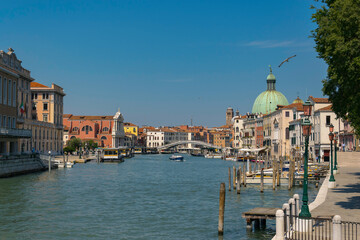 Grand canal in Venice, view of buildings, with docks, boats and bridge in the distance and flying seagull