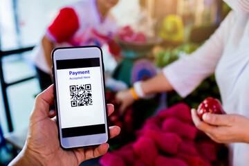 Scanning QR code payment with blurry staff and customer buying fruit in market.