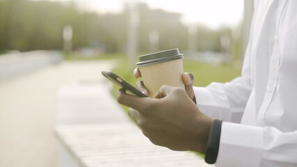 Close up of African American man wearing white shirt drinking coffee and using his phone