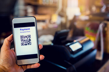 Scanning QR code payment with blurry cashier machine at counter service in coffee shop.