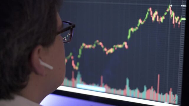 Businessman analyzing a graphic of a stock exchange chart. Back of the head of a young male businessman looking at a stock diagram on the big screen of the computer