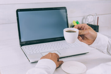 Mock-up Technology. Businessman holds a smartphone in his hands, on a background of laptop and coffee on a wooden table.