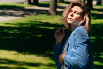 Fashionable girl walks in street park. Concept of developing hair in blonde, model poses for the camera