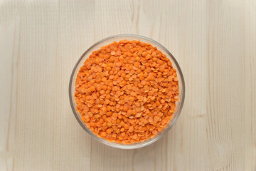 Top view raw orange persian lentil in round bowl on wooden background