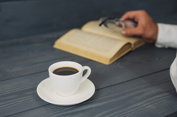 Concept on the topic of education. A man with glasses reads books, on a wooden background with coffee.