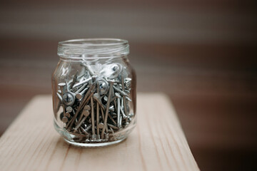 Close up glass jar with metal screws on wood, bokeh background selective and soft focus. Iron...