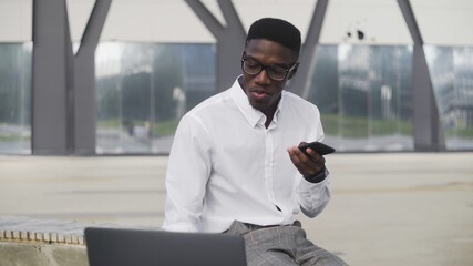 Attractive African Businessman with smart phone looking at notebook and recording voice message in park