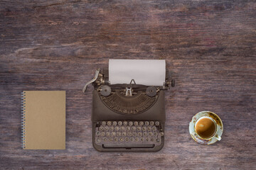 top view photo of vintage typewriter with blank page next to cup of coffee, on wooden table.