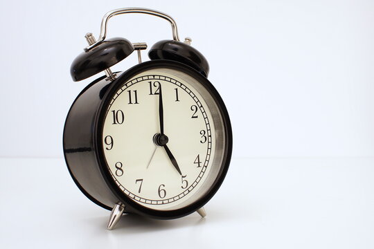 Black vintage alarm clock on table. White background. Wake up concept. An image of a retro clock showing 05:00 pm/am.  