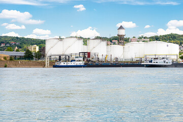 Storage silos, fuel depot of petroleum and gasoline on the banks of the river in western Germany on a beautiful blue sky with clouds. Visible tanker barge.