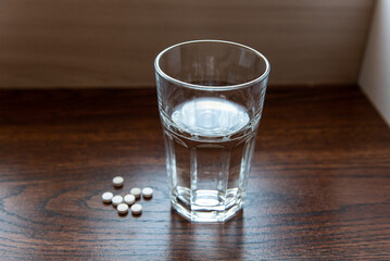 pills lying next to a glass of water on a wooden table
