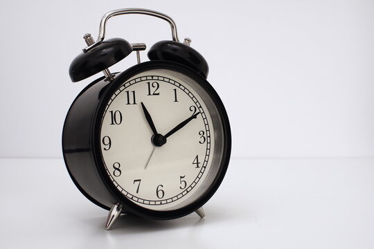 Black vintage alarm clock on table. White background. Wake up concept. An image of a retro clock showing 11:10 pm/am. 