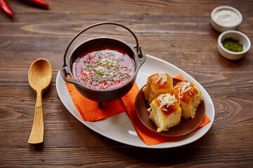 Traditional Ukrainian Russian vegetable borscht on an old wooden background in portioned cast iron. With herbs, sour cream and garlic bread.
