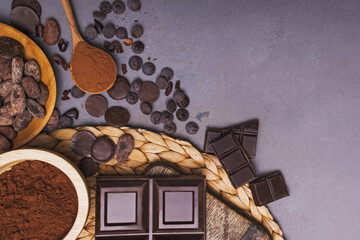 Chocolate pieces and drops, cocoa beans and powder on grey background