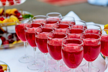 A row of glasses with red drinks, juice, champagne or wine at a party. Catering. Glassware on the table with a white tablecloth. Festive buffet for the holiday.