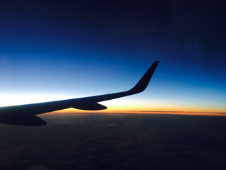 飛行機の窓から見たカラフルな空と飛行機の翼のシルエット