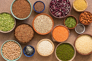 Collection of various of legumes, beans, grains and seeds in bowls on a brown stone background. Top view, flat lay
