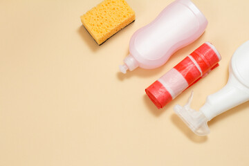 Bottles of dishwashing liquid, garbage bags and sponge on a beige background.