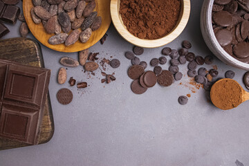 Chocolate pieces and drops, cocoa beans and powder on grey background