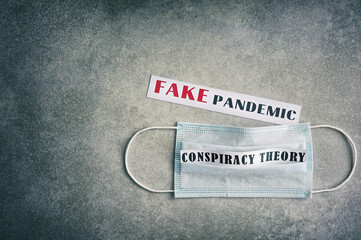 Fake pandemic. Conspiracy theory. Text on a gray vintage background. Vignette. Disposable surgical mask.