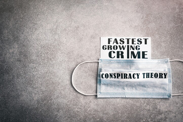 "Fastest growing crime. Conspiracy theory." Black inscription on a gray grunge background with vignette. Medical disposable mask. Global conspiraсу theory.