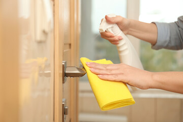 Woman cleaning door handle with rag and detergent indoors, closeup