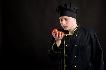 Young male dressed in a black chef suit holding and smells tomatoes