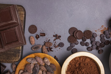 Chocolate pieces and drops, cocoa beans and powder on grey background
