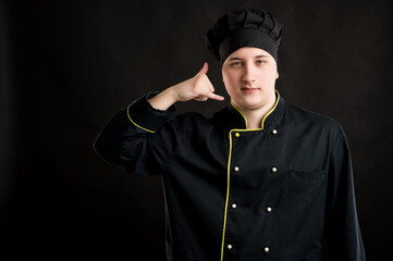Obraz premium Young male dressed in a black chef suit showing call me gesture