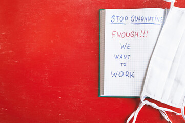 Stop quarantine. Enough. We want to work. Text written in a notebook, white medical protective mask. Red background. Economy crisis. Copy space for text.